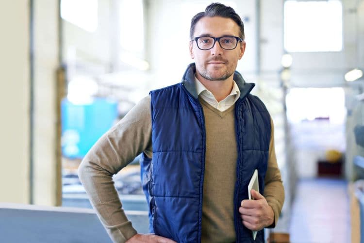 Homme avec des lunettes et en doudoune sans manches qui tient un ipad sous son bras