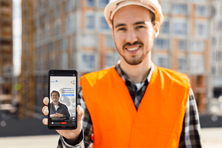 Travailleur avec un gilet de sécurité et un casque nous montre son téléphone avec la vidéo de WeSoft sur la facturation électronique