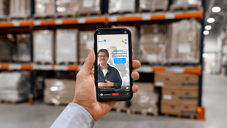 Main d'un travailleur dans un entrepôt, qui nous montre son téléphone. L'écran montre la vidéo de WeSoft sur l'offre proposée à ses clients dans le cadre de la RFE